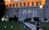 An onlooker at dusk walks towards through a row of candles to view the projection. 
